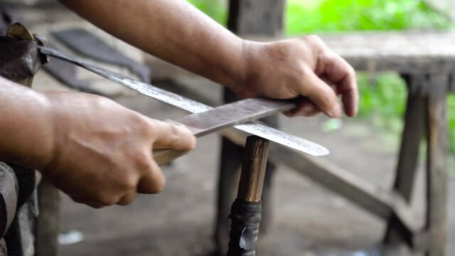 Worker sharpen machete using a file in the forge. Rasp sharpen machete