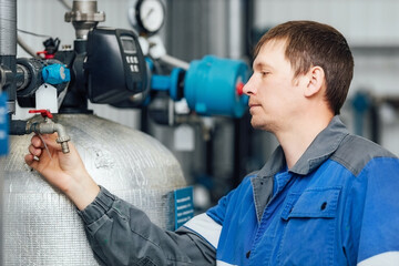An inspector in overalls checks the condition of the water purification equipment. Start-up of the water treatment system. A real worker. - obrazy, fototapety, plakaty