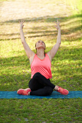 Young smiling woman doing fitness exercises in the park on the green grass with workout clothes