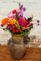 Bouquet of flowers in antique rustic clay jug against white brick wall