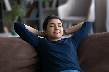 Calm millennial Indian woman rest on comfortable couch in living room sleep or take nap on weekend....