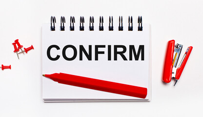On a light background, a red pen, a red stapler, red paper clips and a notebook with the inscription CONFIRM