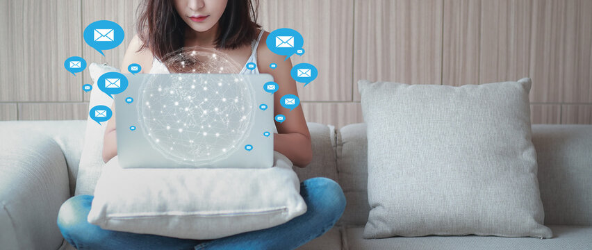Mail communication technology concept. Young woman sitting on sofa using computer receiving and sending e-mail with notification message icons and futuristic graphic world and virtual hologram - Powered by Adobe