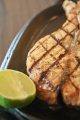 Delicious fish steak served on a hot plate with lemon wedges 