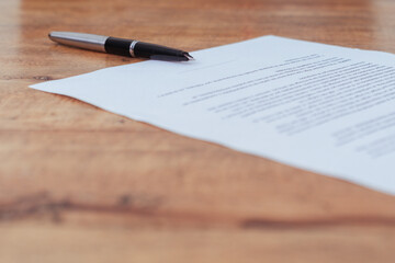 Pen and paper to sign on a wooden table. Concept of legality, contracts and documents