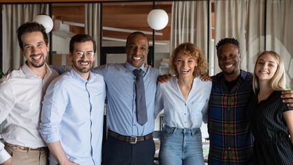 Portrait of overjoyed young diverse multiethnic businesspeople pose together at workplace hug show...