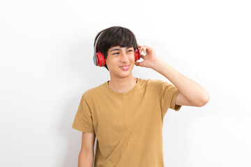 A teenager boy with wireless headphones on his head listens to music on a white background.