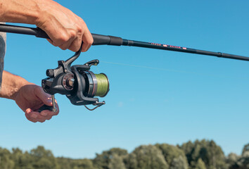 Male hands holding fishing rod or angler over blue clear sky in summer.