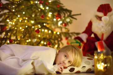 Little boy waiting Santa Claus under tree on Christmas Eve. Santa Claus brought gifts. Child not sleeping, but he does not show it. Magic at Christmas and New Year night.