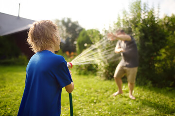 Funny little boy with his father playing with garden hose in sunny backyard. Preschooler child...