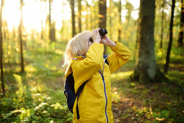 Little boy scout with binoculars during hiking in autumn forest. Child is looking with binoculars....