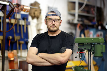 Portrait of handsome metalwork craftsman in protective gloves and glasses working in the workshop....