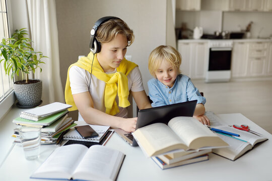 Teenager Boy Study At Home. His Younger Brother Is Playing Near. Homeschooling. Online Education And Distance Learning For Children. Friendship Of Siblings With Big Age Difference.