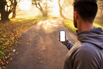 Runner looking on smartphone with empty, blank screen during sunny autumn morning