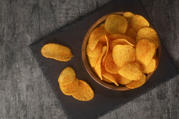 Potato chips with seasonings in bowl on a dark background, top view. Fast food