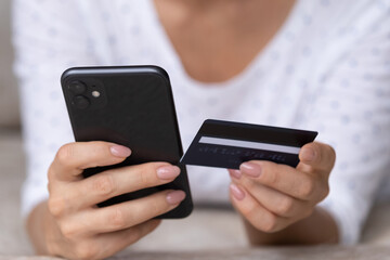 Hands of female customer holding smartphone and credit card, buying on internet stores, using online banking app, paying for purchase on mobile phone. Finance, spending money, ecommerce. Close up