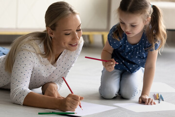 Happy mom teaching little daughter girl to draw with color pencils. Mum and kid relaxing on warm...