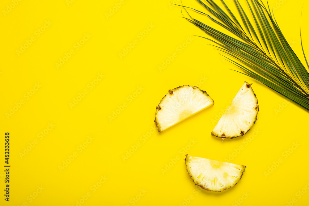 Wall mural ripe pineapple slices, pineapple with foliage and a palm leaf on a yellow background. top view, flat