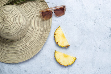 Women's hat, sunglasses, pineapple slices, palm leaf on a concrete background. Top view, flat lay