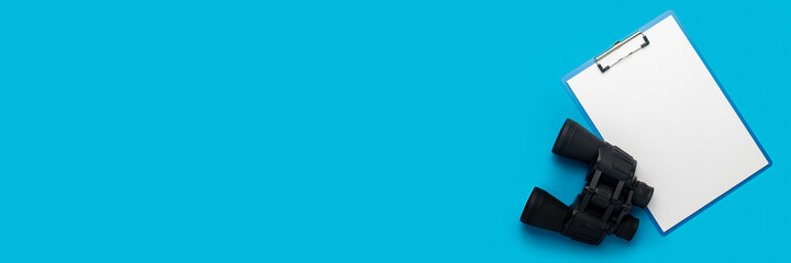 Obraz premium Clipboard with a blank sheet and binoculars on a blue background. Hiring concept, help wanted. Banner. Flat lay, top view