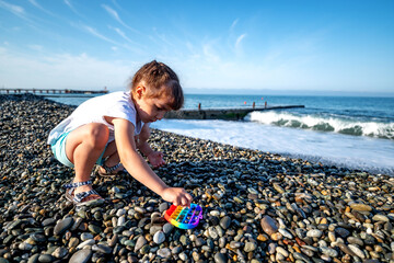 a girl in shorts and a T-shirt plays stones on the seashore and pops it on an early summer morning
