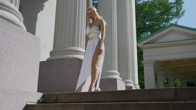 a blonde in a Greek chiton poses for columns. bottom view. the camera is moving