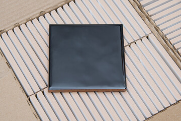 against the background of a box with tile ends, there is a sample of a black square square