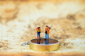 Miniature people Group of young tourist traveler traveling standing on golden compass travel around...