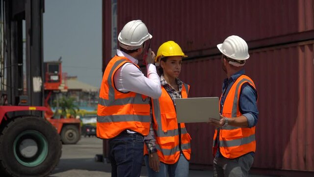 group of harbor worker with foreman talking on the walkie-talkie control loading Containers box and using laptop computer checking list inventory  at warehouse logistic in Cargo freight ship