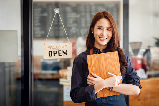 Small business owner at entrance looking at camera in an apron, the owner of the cafe stands at the door with a sign Open waiting for customers. Small business owner concept, 