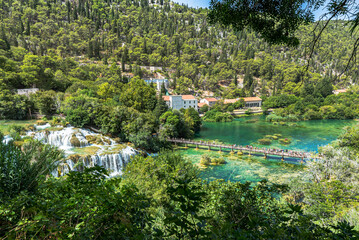 Top view of the beautiful waterfall flowing into the transparent turquoise water lake and tourists enjoying the view at the Krka National park. Croatia 2021