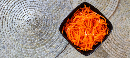 Close-up top view of square ceramic black dish or bowl with Korean carrot salad cut into...