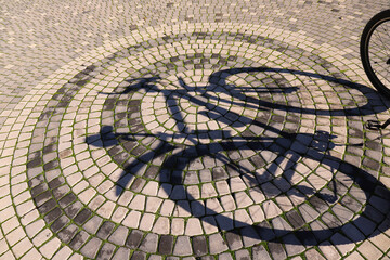The shadow of a bicycle on the cobbled pavement.