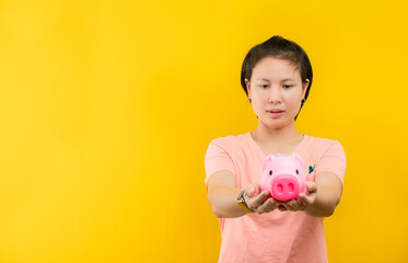 Young woman happily holding a pink piggy bank collecting money is displayed against a yellow background.concept saving.