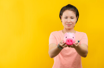 Fototapeta na wymiar Young woman happily holding a pink piggy bank collecting money is displayed against a yellow background.concept saving.