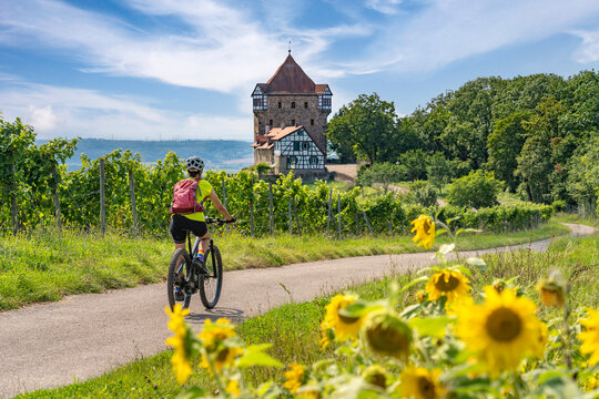 happy senior woman riding her electric mountain bike on sunny  day in the Bottwartal Valley with beautiful medieval castle in the background, Beilstein near Heilbronn, Baden-Wuerttemberg, Germany