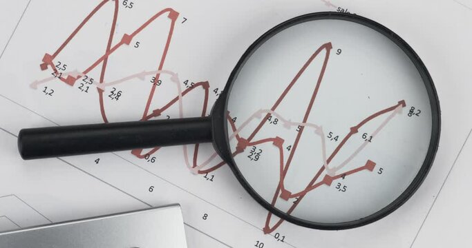 Rotation of a magnifying glass and a calculator lying on a red chart. Business background