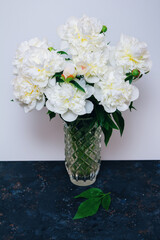 Beautiful white peony flowers bouquet with water drops on petals in glass vase on a table