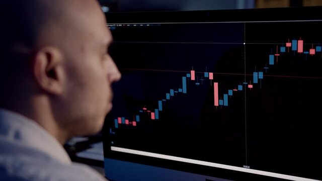 Stock trader with bar charts rise and fall, stock market on computer screen. Blurred man with bald head carefully studying the screen with stock graphs, gimbal shot