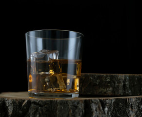 A glass with whiskey and ice cubes stands on a wooden bar