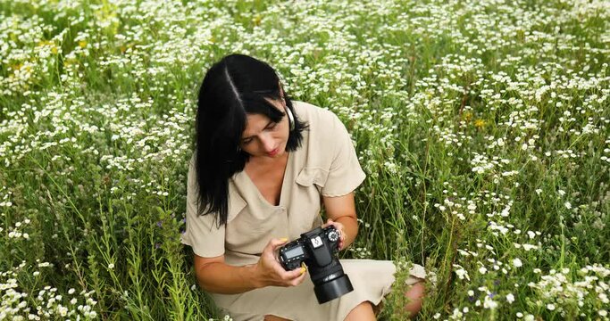 Female photographer sitting outdoors on flower field landscape and looking on the photo on the camera,, woman hold digital camera in her hands. Travel nature photography, space for text, top view.