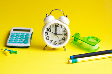 Clock, calculator and stationery on a yellow background