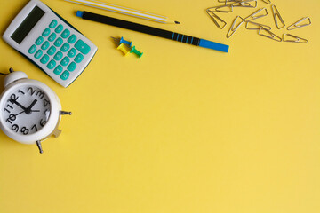Alarm clock, calculator and stationery on a yellow background, copy space