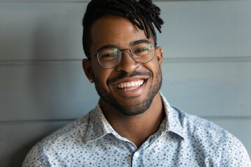 Head shot of happy handsome African American guy with trendy haircut and dreads, black stubble, stylish glasses, looking at camera with toothy smile. Millennial young man, student close up portrait