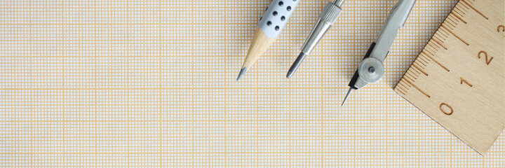 Wooden ruler, compasses and pencil lie on graph paper