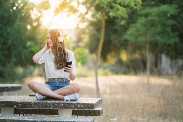 Chica joven al atardecer en un parque natural con smartphone y cascos