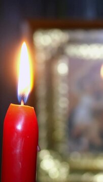 Candles are burning in dark against blurred Virgin Mary icon. Religion and spirituality. Selective focus. On dark background. Vertical video. Close-up.
