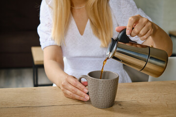 Girl pours coffee from a stylish moka pot into a cup. Equipment for making coffee. Morning coffee for breakfast. Fragrant black coffee in a cup close up