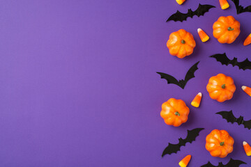 Top view photo of halloween decorations small pumpkins candy corn and bats silhouettes on isolated violet background with copyspace