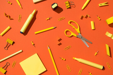 Top view photo of scattered yellow stationery school accessories scissors pencils markers binder clips pushpins and sticky note paper on isolated vivid orange background